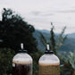 Two bottles of fermenting coffees with a scenic background of trees and mountains.