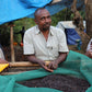 Mustefa Abakeno and coffee farmer neighbors around an outdoor raised drying bed with a green cloth holding dried coffee cherries.