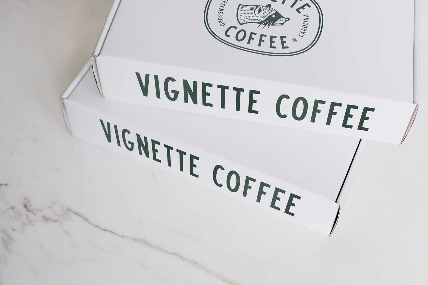 White Boxes featuring Vignette Coffee written in sans serif black letterings. A raccoon logo on top.